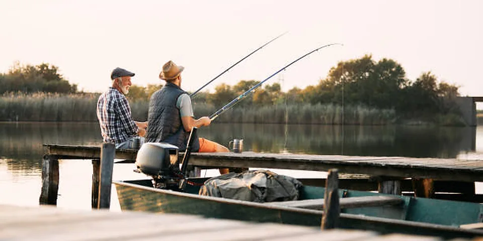 Two different sized fishing rods on an empty dock beside calm water