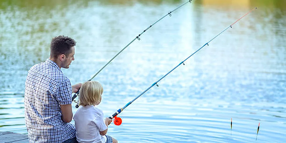 Two different sized fishing rods on an empty dock beside calm water