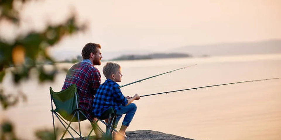 Two different sized fishing rods on an empty dock beside calm water