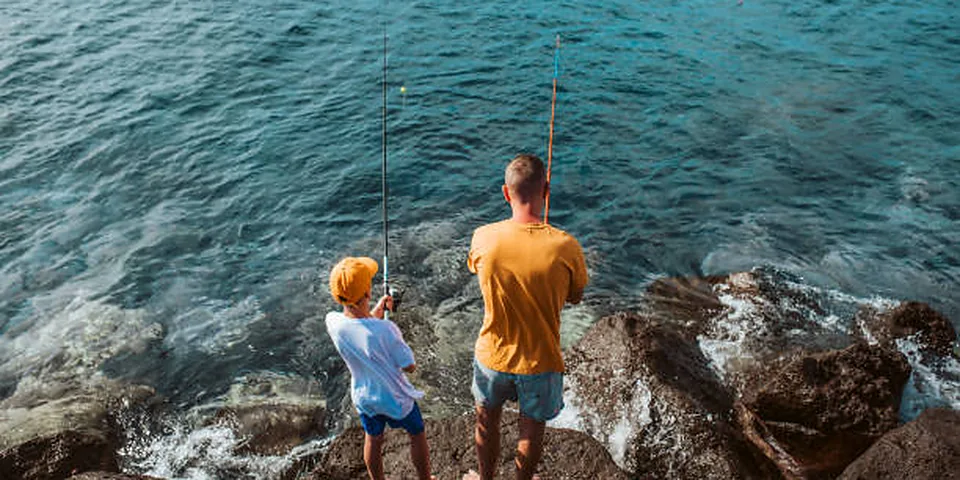 Two different sized fishing rods on an empty dock beside calm water